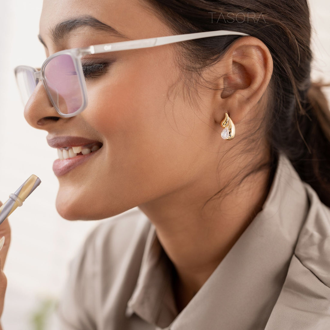 Pair of Rain Drop golden and silver earrings on a dark surface with a phone and TASORA branding in the background.