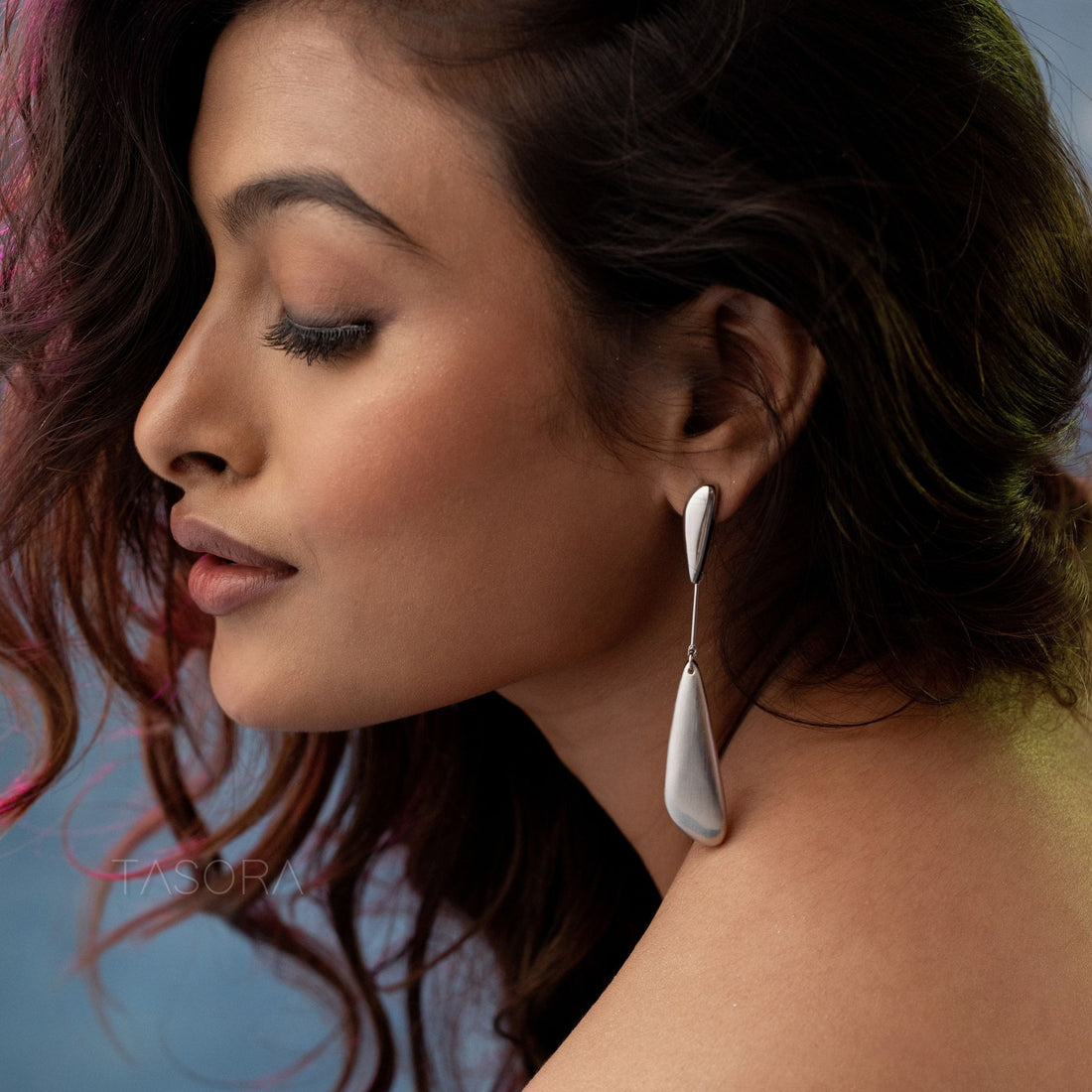 Gold and silver Sleeky Drop earrings on a stone surface with 'TASORA' branding.