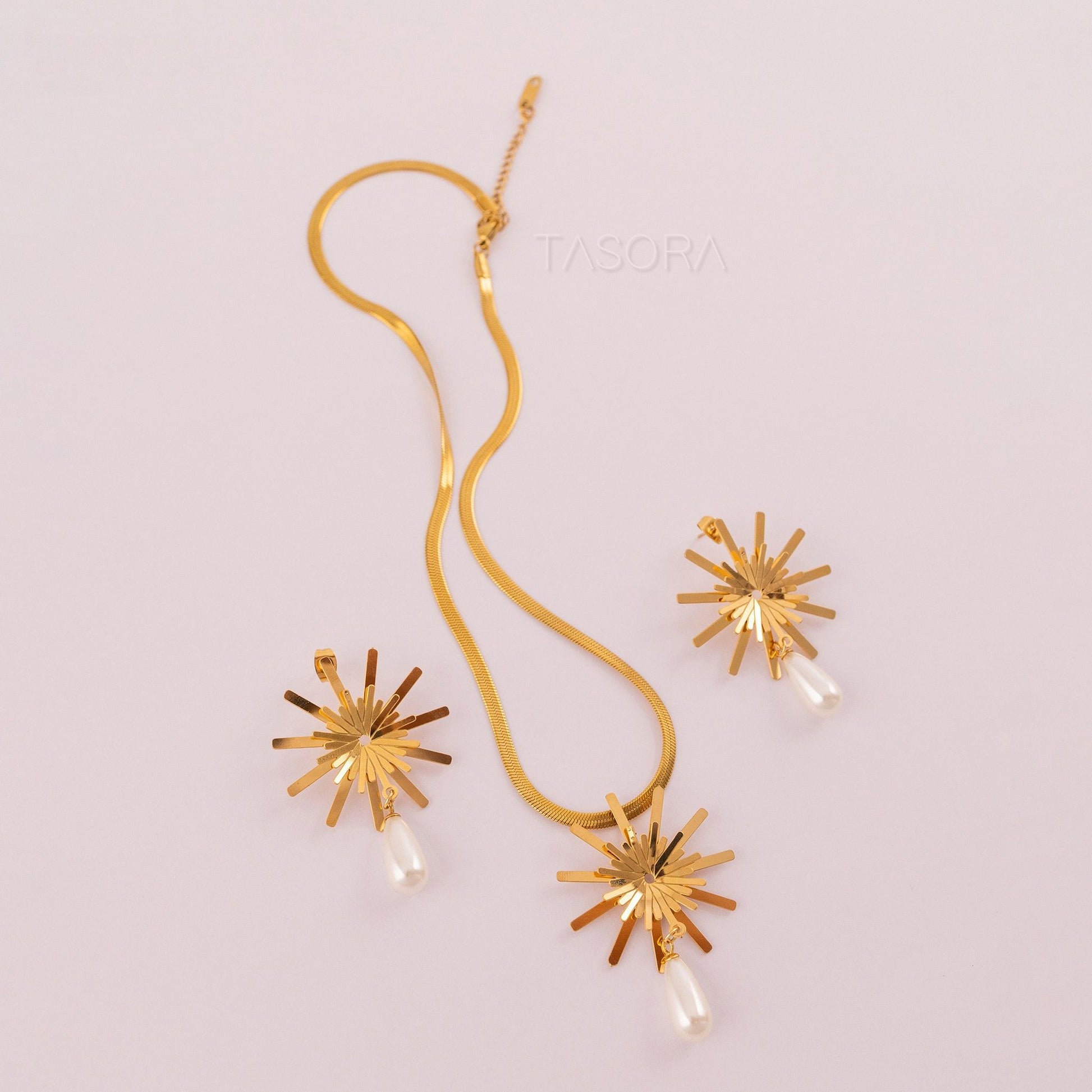 Golden Solara Bloom necklace with starburst designs and pearl drops on a light pink background, featuring the brand 'TASORA'.
