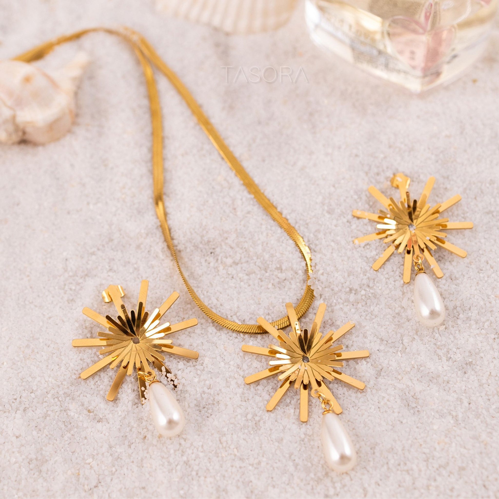 Golden Solara Bloom necklace and earrings with pearl drops on a sandy background with TASORA branding