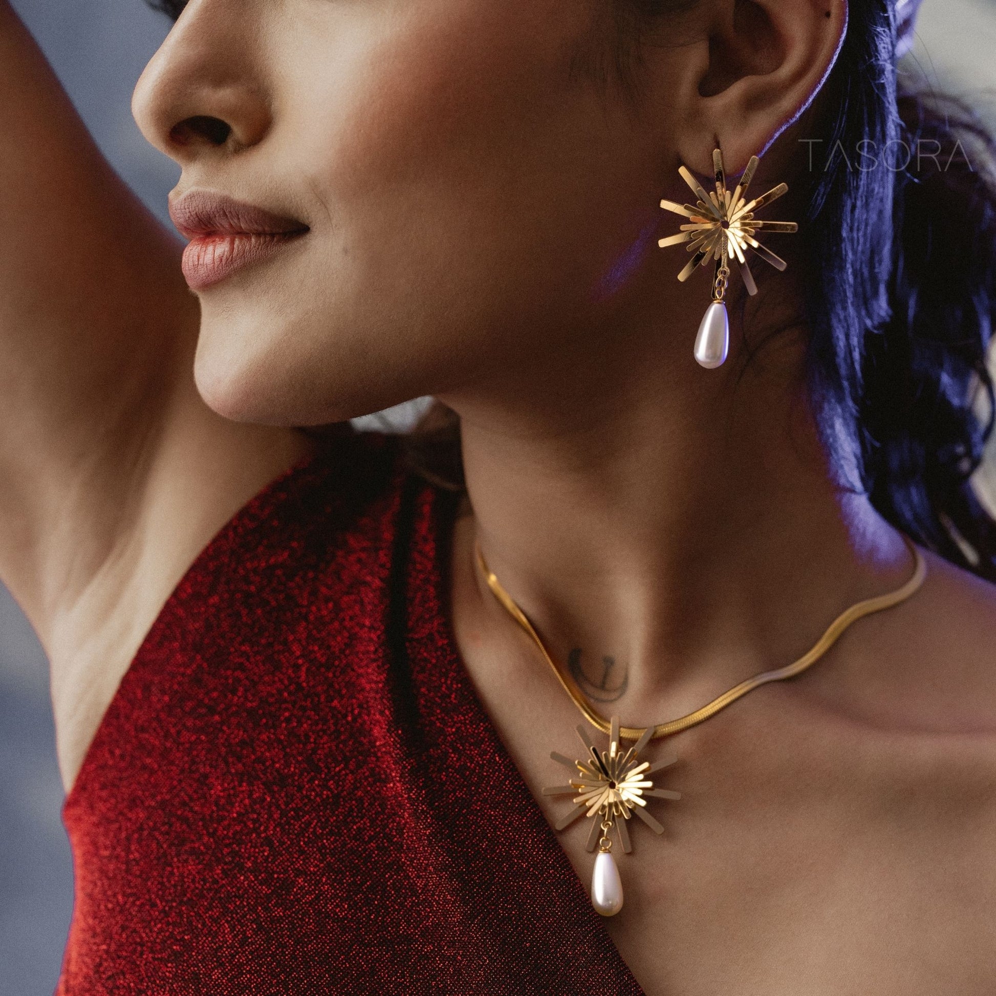 Close-up of a woman wearing golden Solara Bloom earrings and necklace by TASORA with a blurred background