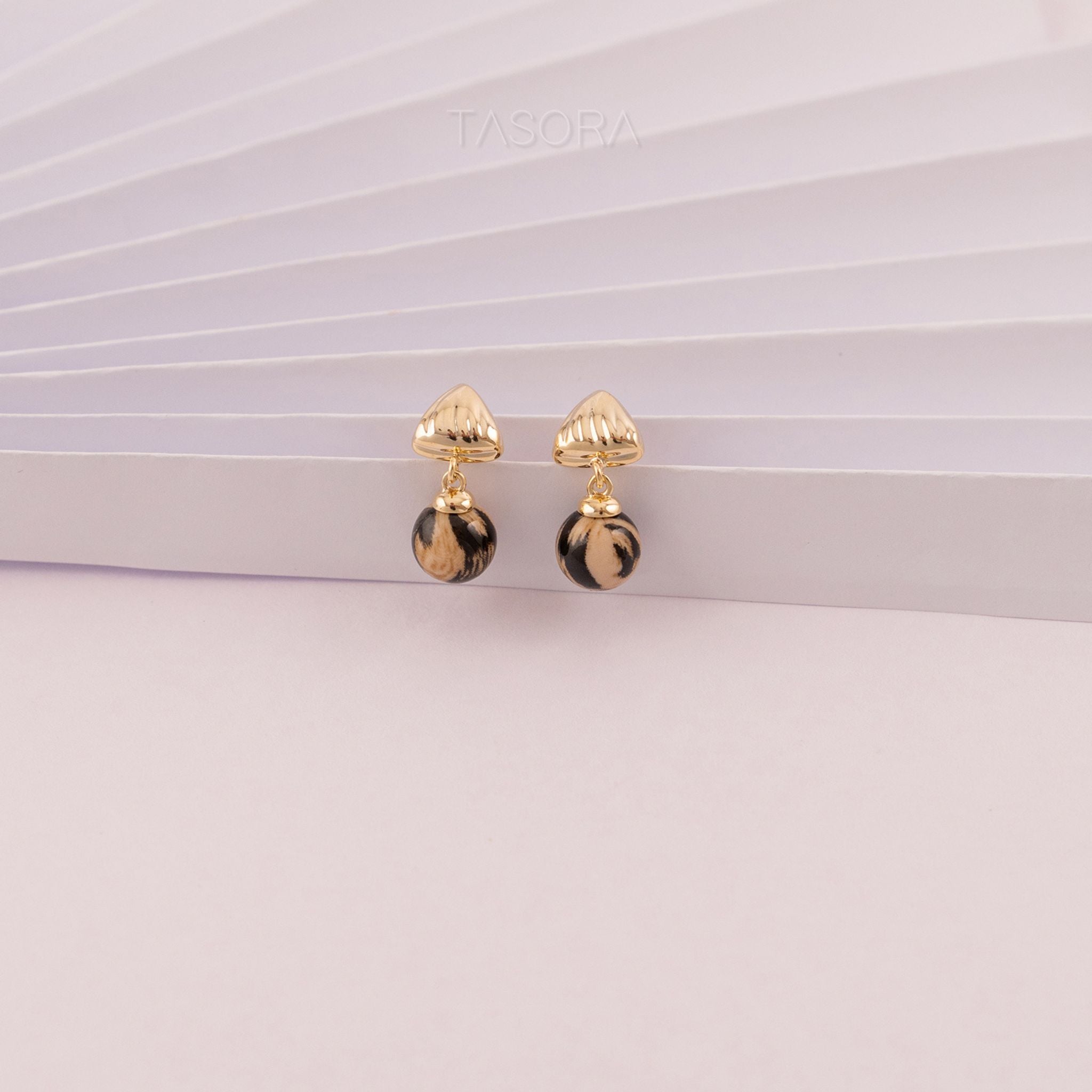 Sona Halo Biege earrings with black accents on a white paper surface with TASORA branding