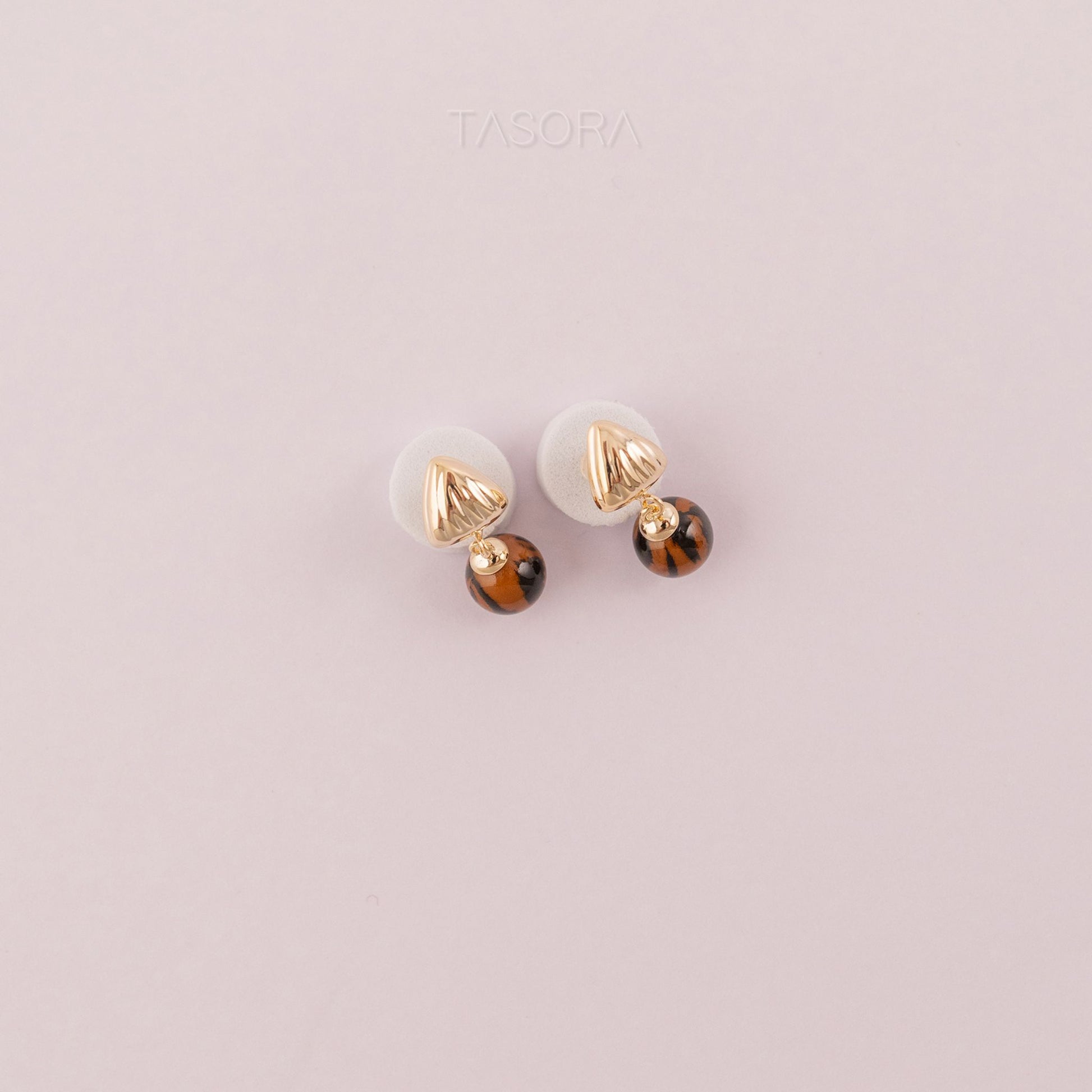Pair of Sona Halo earrings of TASORA brand with gold and brown accents on a light pink background