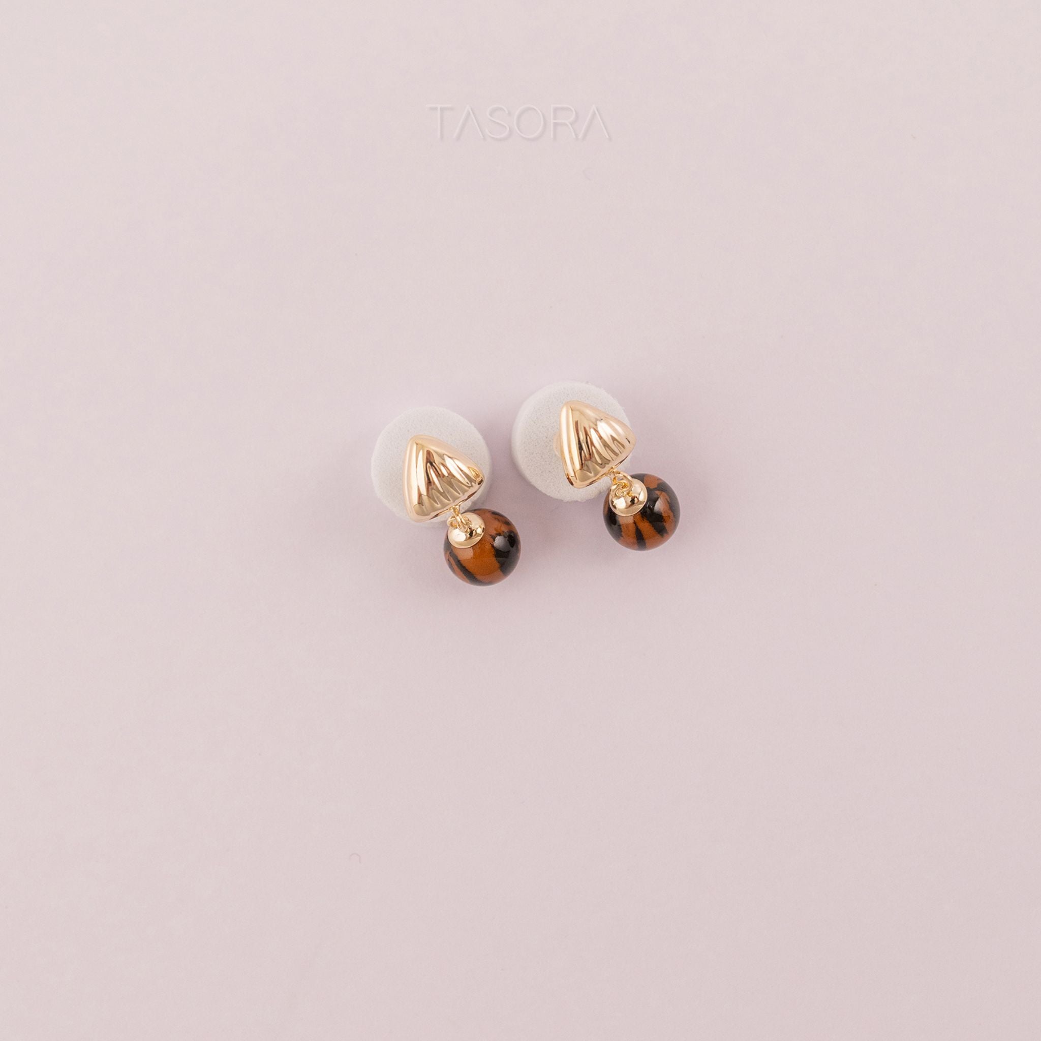 Pair of Sona Halo earrings of TASORA brand with gold and brown accents on a light pink background