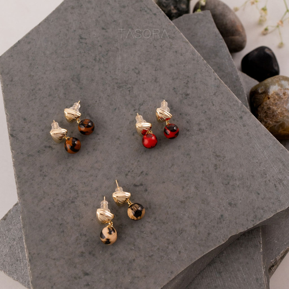 Pairs of Sona Halo earrings of TASORA brand on a gray stone surface.