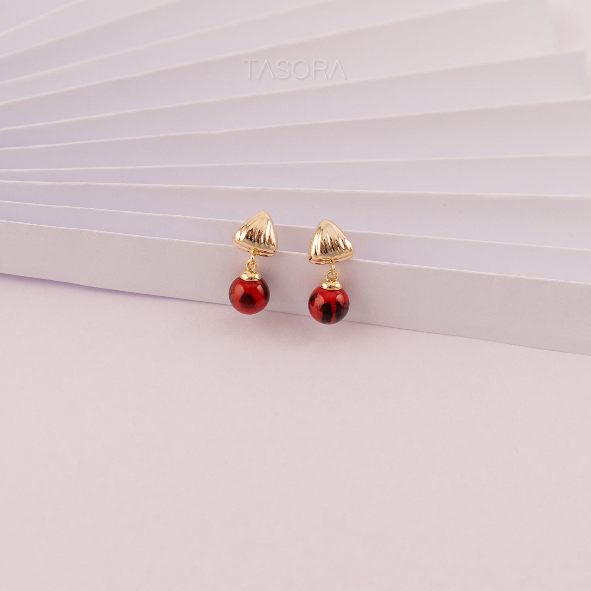 Pair of red Sona Halo earrings with TASORA branding on a light pink background