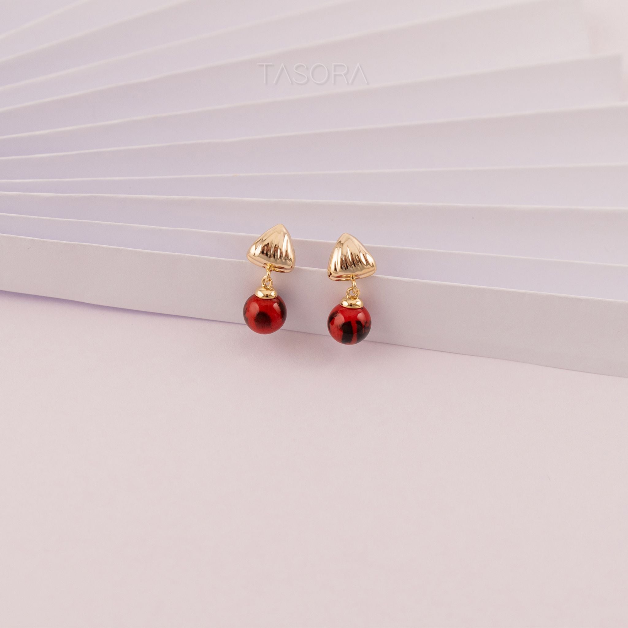 Pair of red Sona Halo earrings with TASORA branding on a light pink background