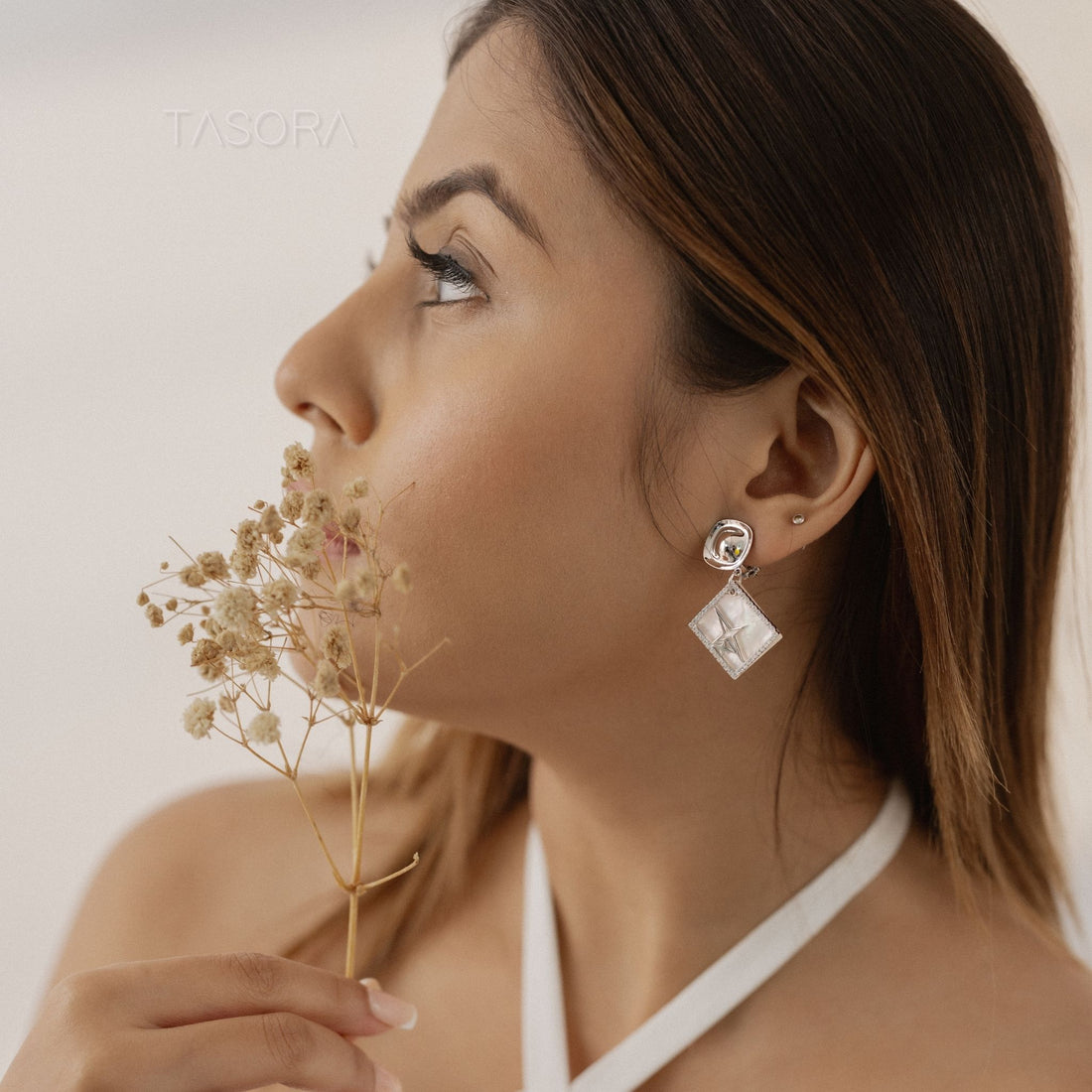 Silver Starlit Gleam earrings with star designs on a beige fabric background with TASORA branding