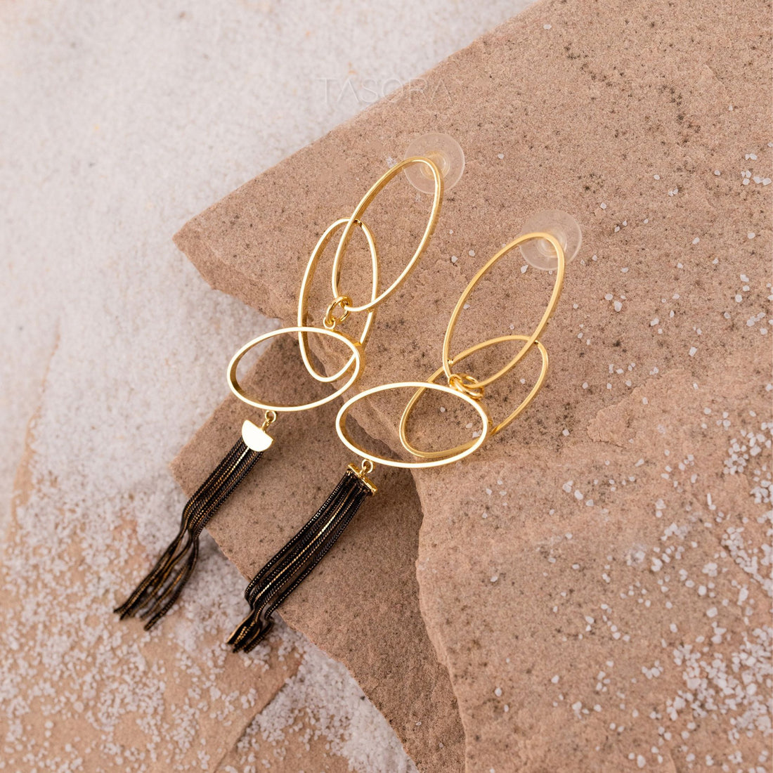Twilight Threads Golden earrings with tassels on a textured beige stone surface with TASORA branding