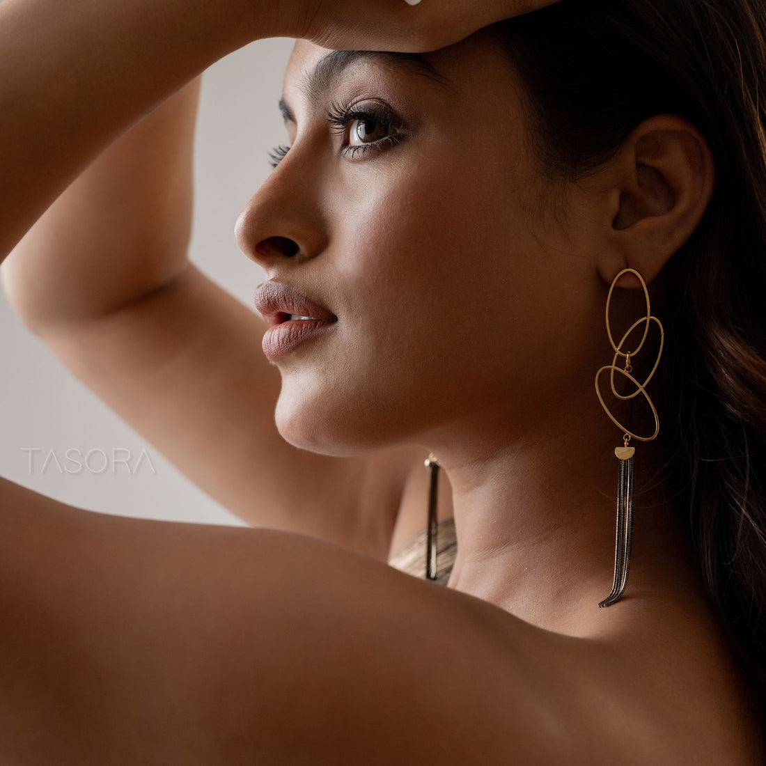 Twilight Threads Golden earrings with tassels on a textured beige stone surface with TASORA branding