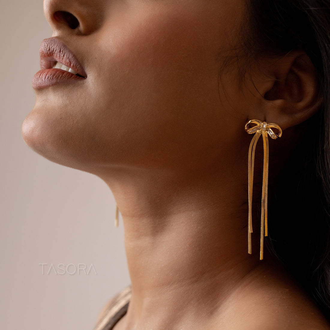 Silver and golden Twinkle Tie earrings by TASORA with bow details on a white fabric background