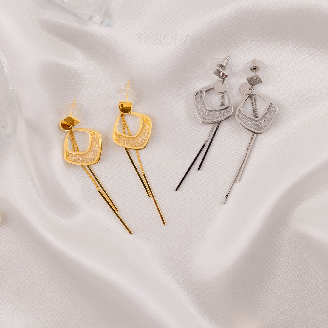 Two pairs of Viola Threads earrings by TASORA, one gold and one silver, on a white fabric background.