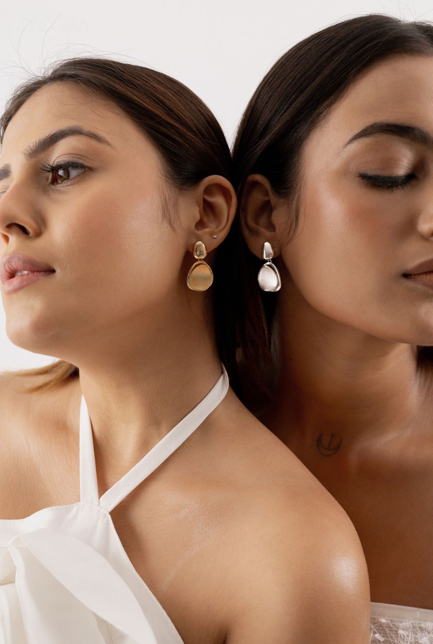 Two women wearing pebble Huggies Earrings of TASORA brand with a neutral background
